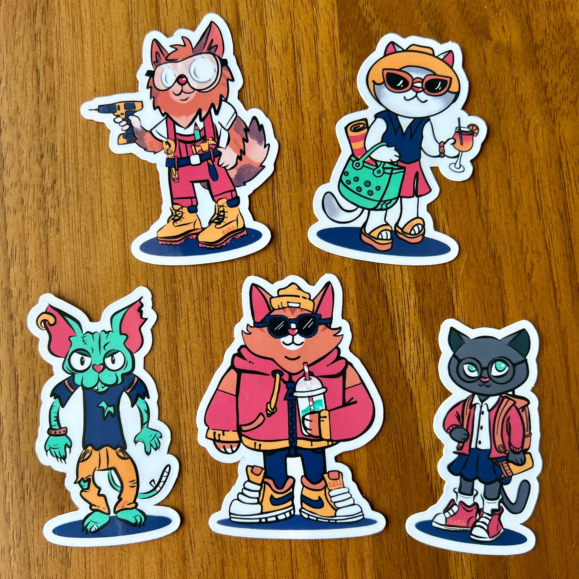 Five cat cartoon character stickers on a wooden surface
