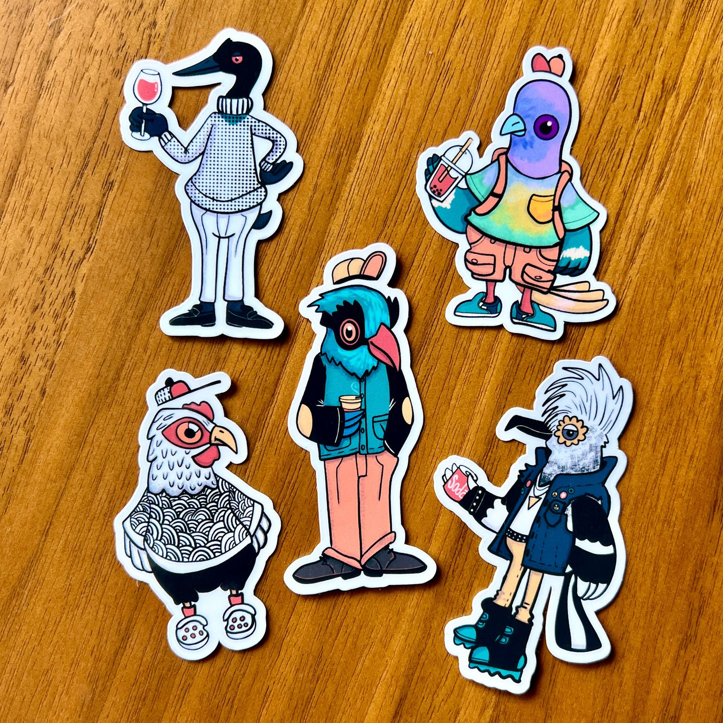 Five colorful bird cartoon character stickers on a wooden surface